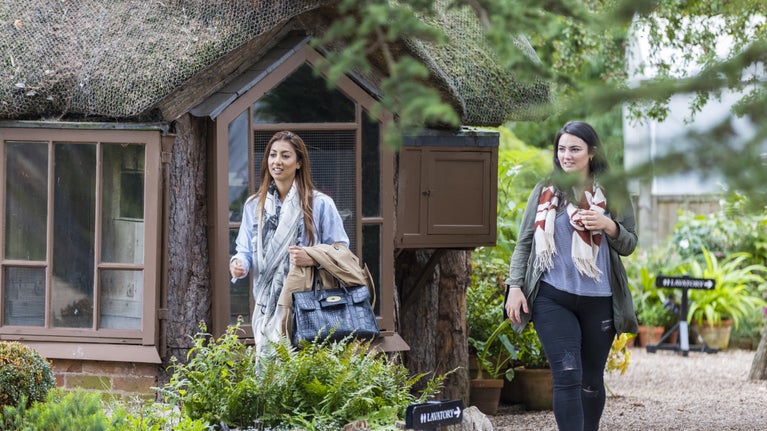 Two visitor exploring the garden with the Victorian summer house visible behind them and potted plants in bloom